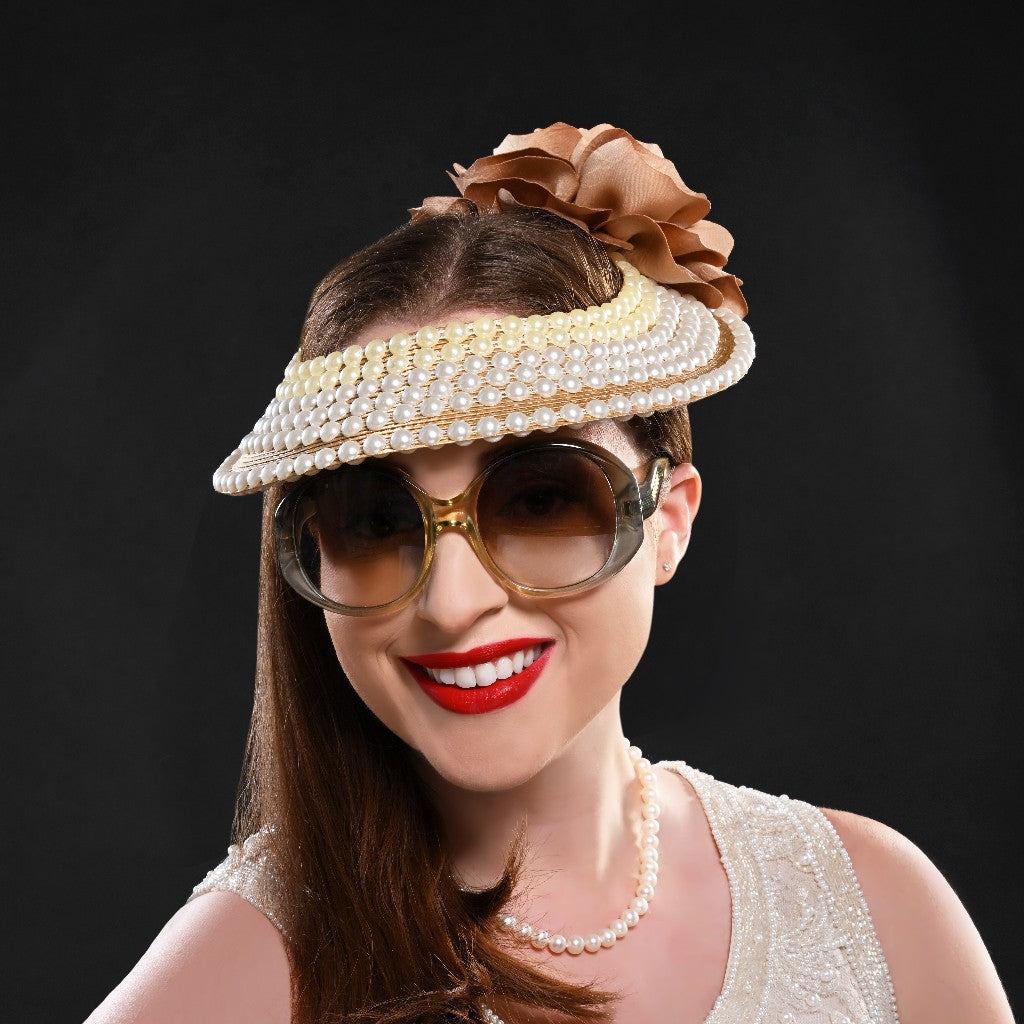 A woman wearing a white open top fascinator adorned with pearls and gold trim, topped with a large satin flower.