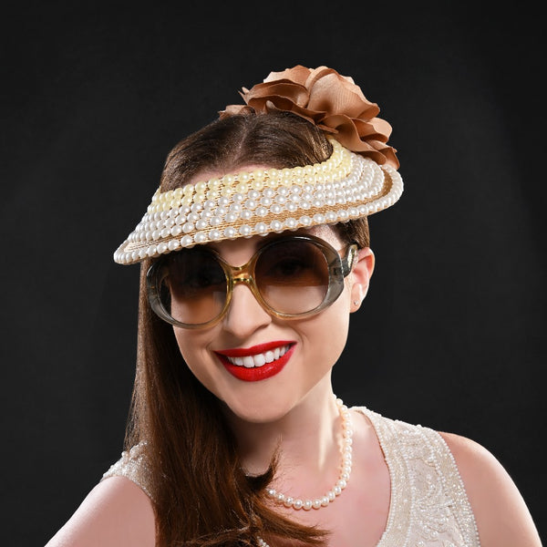 A woman wearing a white open top fascinator adorned with pearls and gold trim, topped with a large satin flower.
