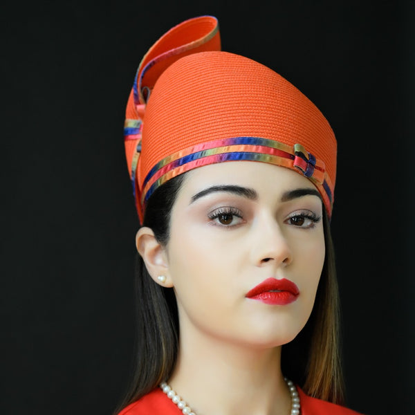 A woman wearing an orange pillbox dress hat with a colorful ribbon around the base.