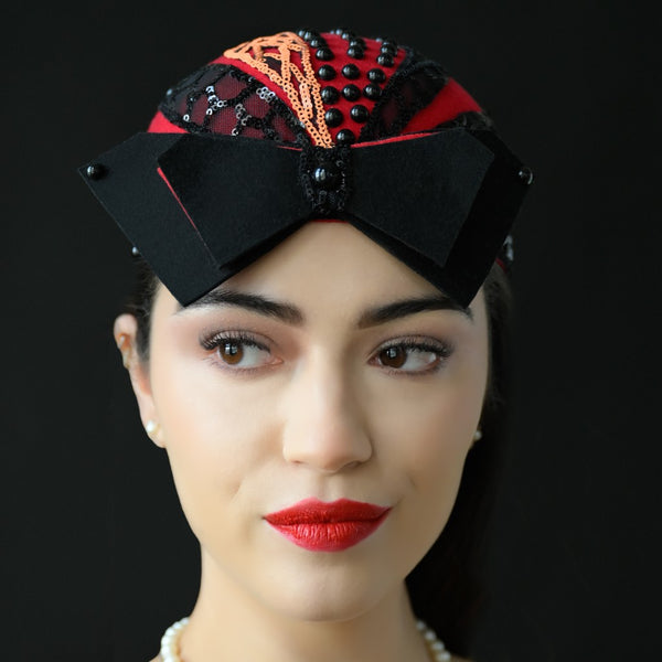 A person wearing a red and black wool fascinator with sequins and black pearls.